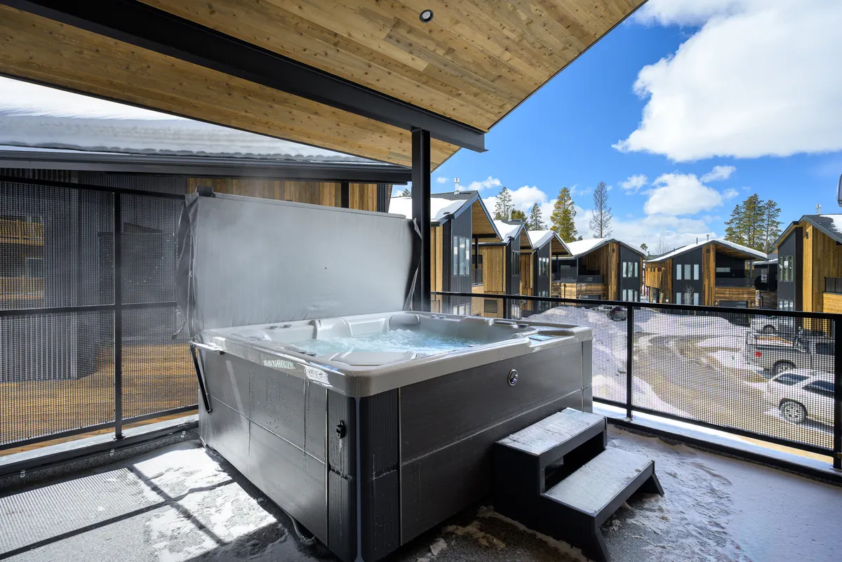 This exterior image highlights a private hot tub set on a wooden deck, surrounded by neighboring cabins and natural scenery. People are relaxing in the hot tub, soaking in serene sunset views and enjoying the peaceful ambiance with friends or family.