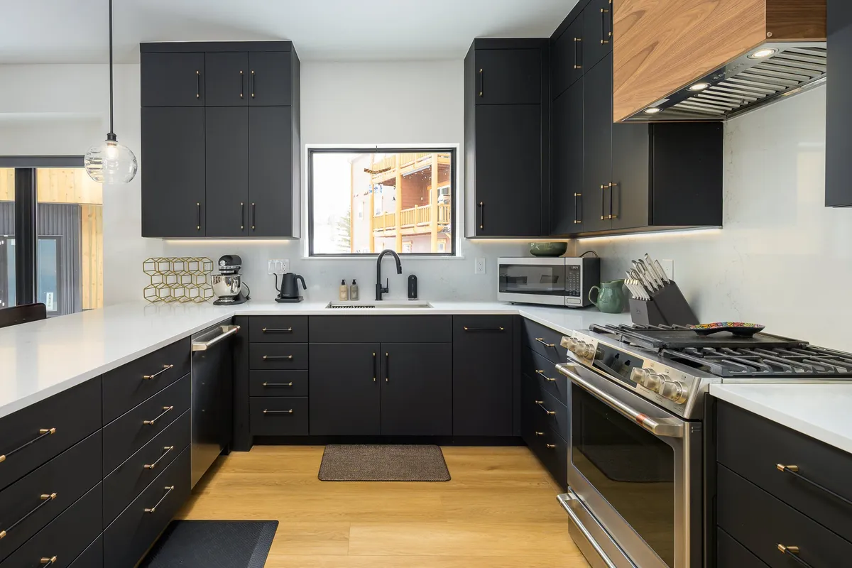 A sleek, modern kitchen with a central island, dark cabinetry, and stainless steel appliances, all illuminated by ample natural light from a large window. The space feels contemporary and functional, highlighting efficient modern appliances and a setting designed for gatherings.