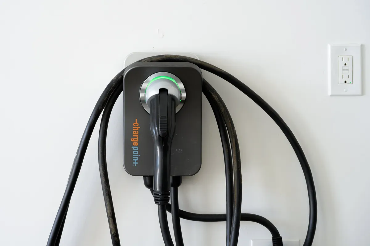 An interior scene focusing on a dedicated electric vehicle charging station in the garage. The image shows the EV charger, cables, and wall socket, highlighting the villa's commitment to sustainability and convenience for guests with electric cars.