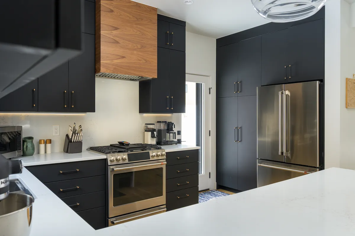 A contemporary kitchen scene highlighting stainless steel appliances, dark cabinetry, a wooden hood, and a marble countertop. The space feels functional yet stylish, set up for both cooking and entertaining family or guests.