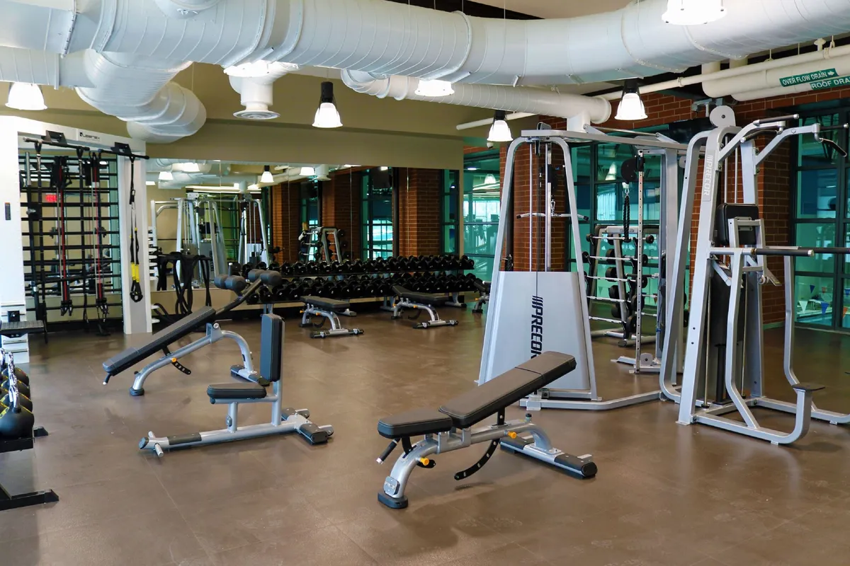A well-equipped fitness center with weight benches, cardio machines, and a full dumbbell rack. The bright, energetic atmosphere encourages guests to stay active regardless of the season.