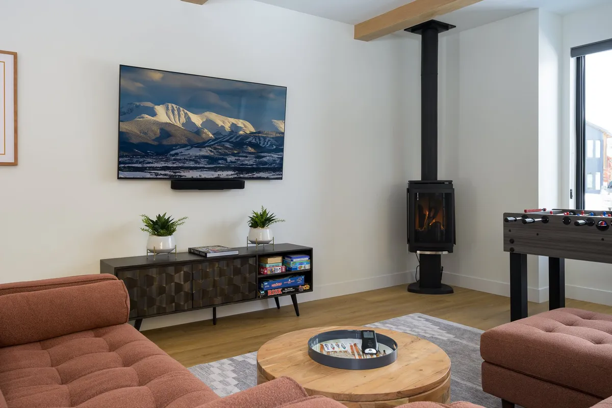 A cozy living room with a plush sofa, coffee table, large television, fireplace, and foosball table. The setting invites relaxation, game nights, and gatherings—perfect for unwinding after outdoor excursions.