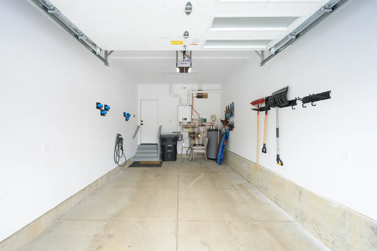 A functional, organized garage with a clean concrete floor, visible storage tools, a utility door, and a garage door opener. The space is set up for storing gear—ideal after days spent hiking, biking, skiing, or snowshoeing.