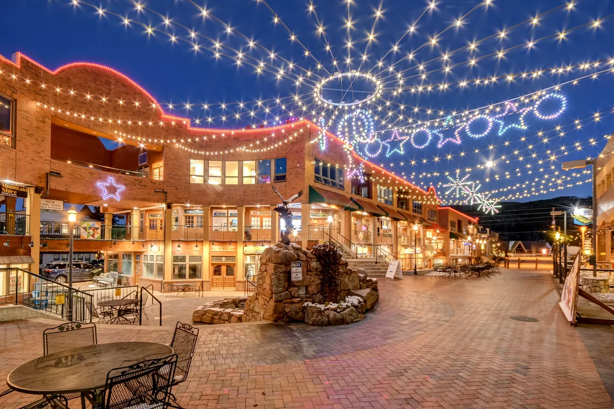 This exterior image captures a lively outdoor setting with twinkling string lights, decorative stars, a stone fountain, and inviting outdoor seating. The scene is festive and welcoming, suggesting community gatherings and a vibrant atmosphere that extends the villa experience beyond its walls.