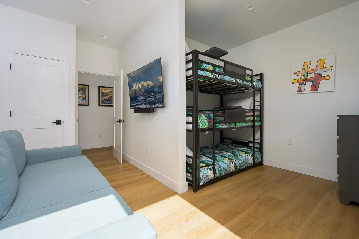 A playful and comfortable bunk room featuring a bunk bed, sofa, wall-mounted television, and whimsical artwork. The space balances fun and relaxation, making it ideal for families or groups.