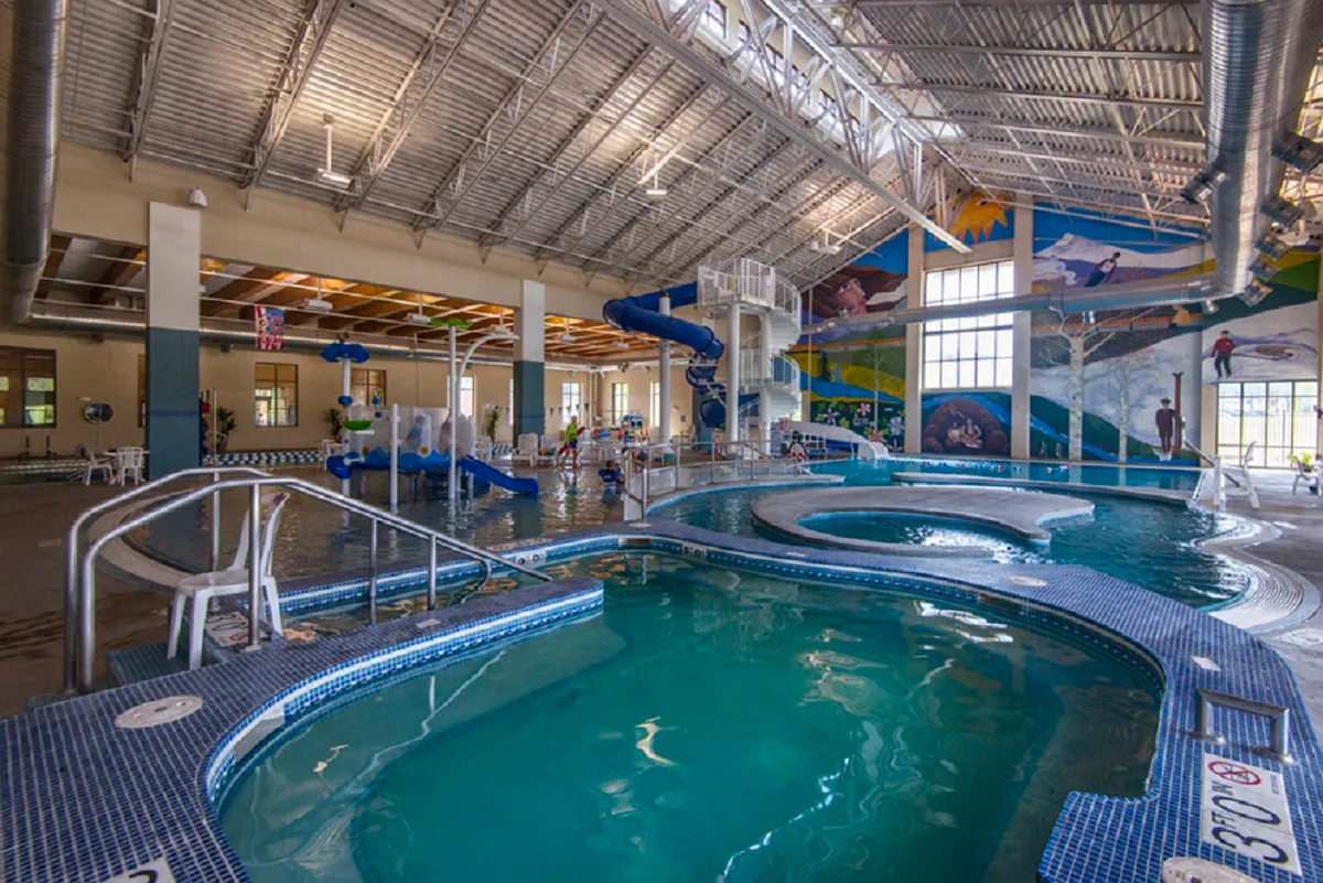 An inviting indoor aquatic center features a sparkling pool, a colorful water slide, joyful children playing in the water, and lively murals. The environment radiates energy and fun, with families engaging in playful activities and making memories together.