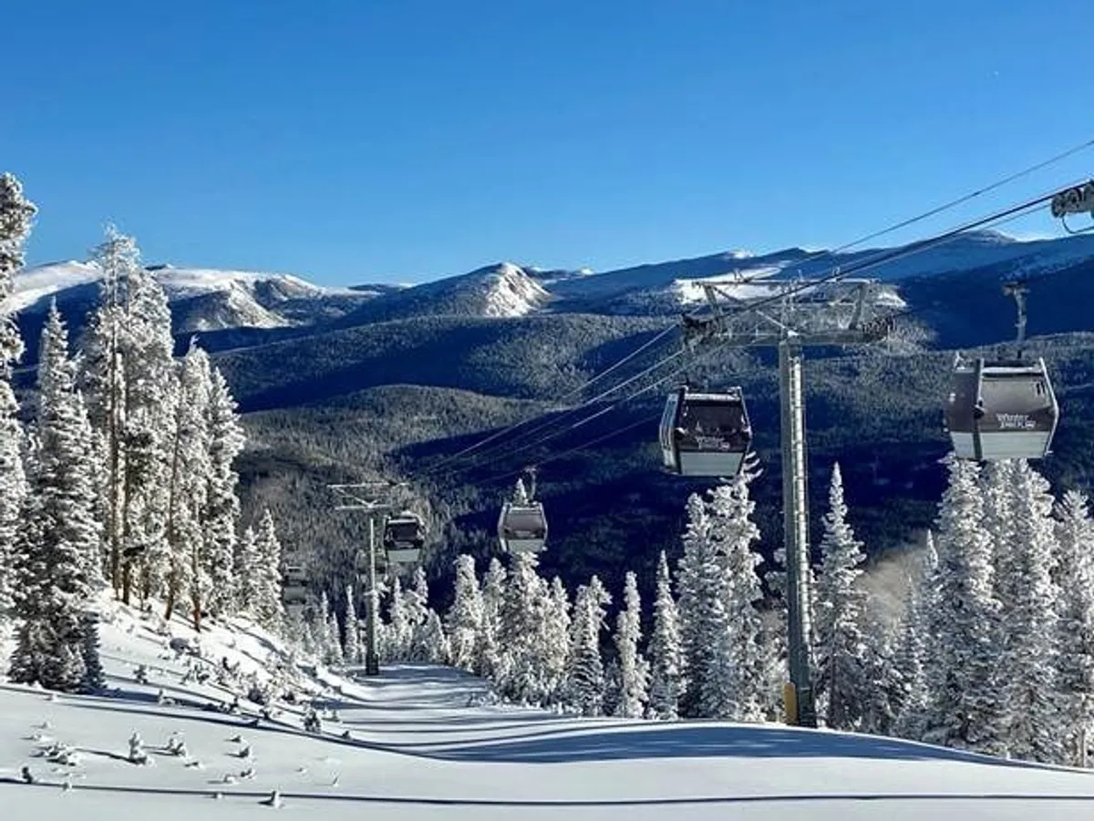 A panoramic view of snow-covered Rocky Mountain slopes with gondola lifts gliding overhead and distant mountain ranges. The scene is bathed in crisp daylight, inviting guests to partake in adventurous activities like skiing and snowboarding.
