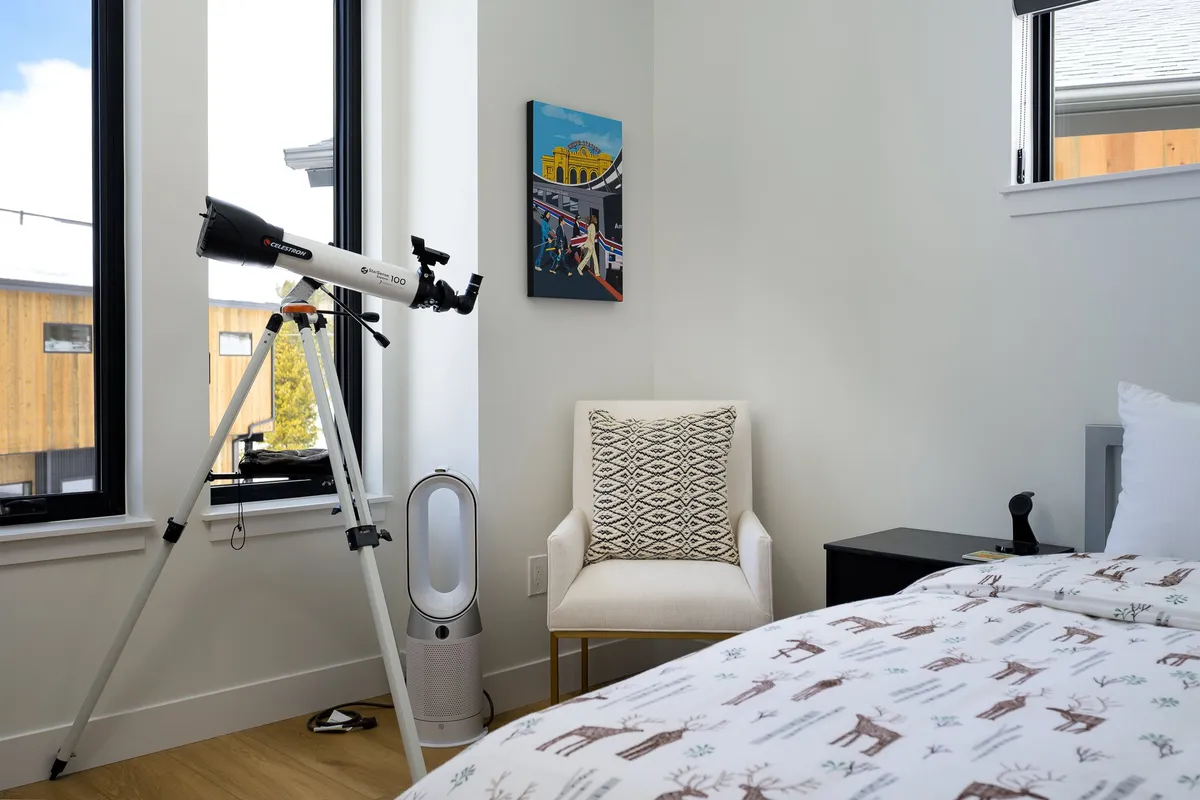 A tranquil bedroom featuring a telescope set up by the window, an armchair for relaxing or reading, and soft, natural light spilling onto a cozy bed. Subtle artwork adds a touch of inspiration, inviting moments of stargazing or quiet contemplation.