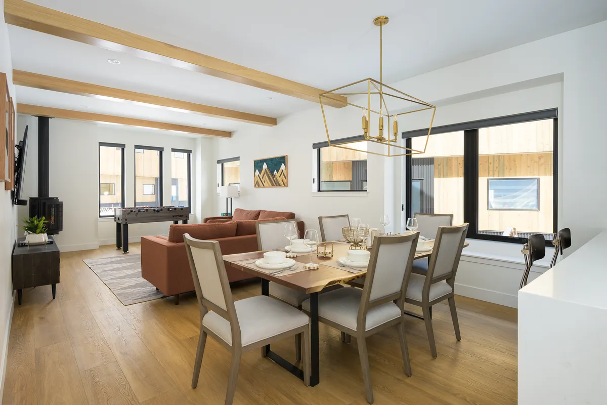 The photo captures a seamless flow between the dining area and living space, with a set dining table, cozy sofa area, and expansive windows that invite in natural light. The inviting atmosphere sets the stage for shared meals, socializing, and family game nights.